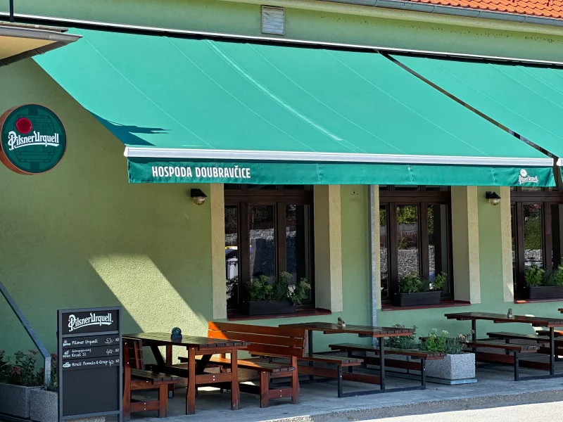 Venkovní posezení pod zelenou markýzou s logem Pilsner Urquell